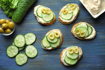 Composition of tasty sandwiches with fresh cucumber on wooden background