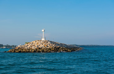 White  lighthouse in the sea in day time and blue sky background . 