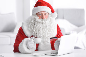 Santa Claus with laptop and credit card drinking coffee at home