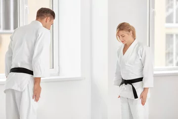 Crédence de cuisine en verre imprimé Arts martiaux Young man and woman performing ritual bow prior to practicing karate in dojo