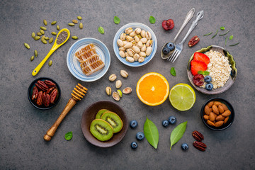 Ingredients for the healthy foods background Mixed nuts, honey, berries, fruits, blueberry, orange, almonds, oatmeal and chia seeds .The concept of healthy food set up on dark stone background.