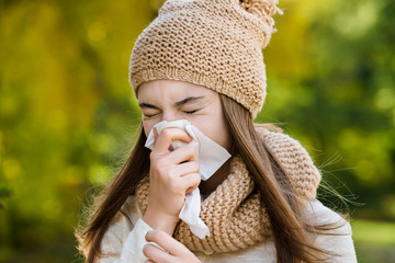 Young woman sneezes in a handkerchief on the street in autumn