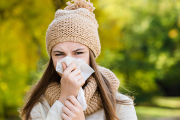 Young woman sneezes in a handkerchief on the street in autumn