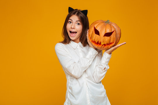 Excited teenage schoolgirl in uniform holding halloween pumpkin