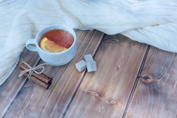 Tea with lemon in white cup, knitted woolen scarf on a wooden table, frost effect. Copy space