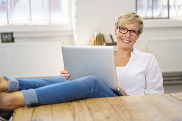frau sitzt zuhause am tisch und arbeitet entspannt am laptop