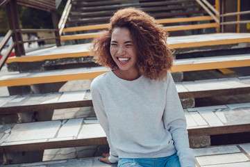 Curly haired girl with freckles in blank grey sweatshirt on the street. Mock up.