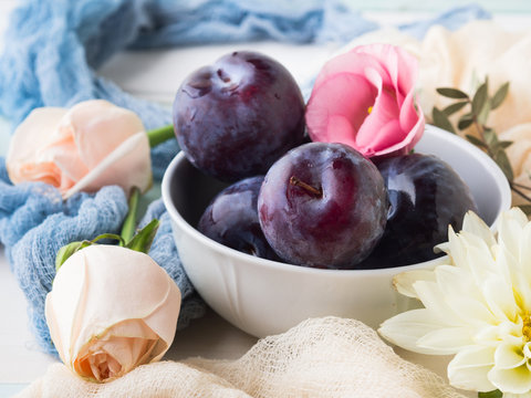 Blue plums in bowl with pink flowers. Summer autumn fruit