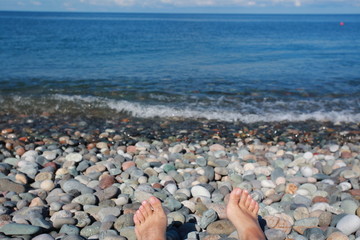 feet of a woman resting sunbathing on a pebble beach by the sea