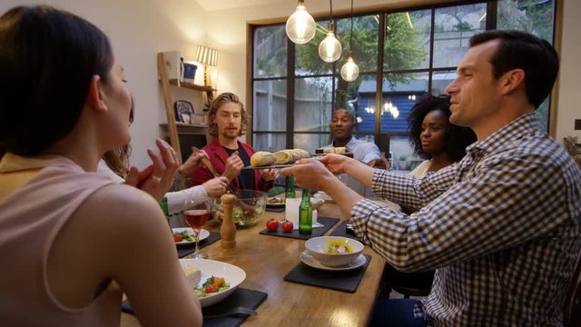 Happy mixed ethnicity group of friends enjoying dinner party with drinks in modern home.
