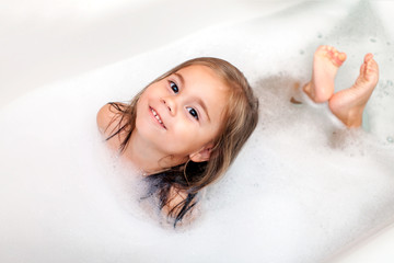 happy little girl is taking a bath with a foam