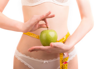 Fitness woman in panties with beautiful body shows green apple and measures waist