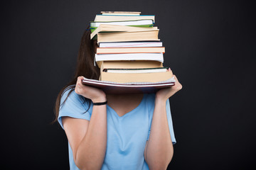 Young student hiding behind her school books