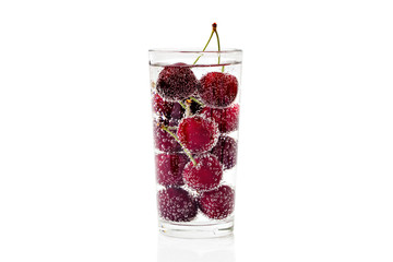 Cherries in a transparent glass with sparkling water isolated on white background