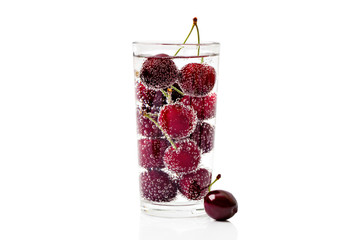 Cherries in a transparent glass with sparkling water isolated on white background