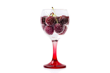 A glass of wine filled with sparkling water and berries of a ripe cherry isolated on a white background