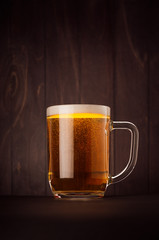 Mug beer glass with golden sparkling lager on dark wood board, vertical. Template for advertising, design, branding identity, restaurant menu, cover.