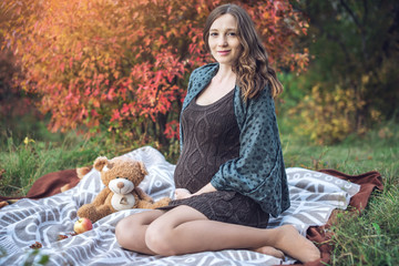Expectant mother with a tummy sits on a blanket and tells stories to the baby. Concept of pregnancy and autumn harmony