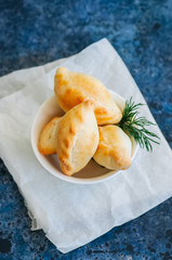 Small mashed potato pasties (hand pies) in a white bowl on a baking paper. Blue stone background.