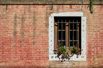 Fototapeta na wymiar Window with lattice and flowers on the brick wall.Italy