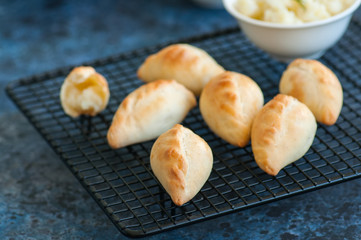 Small mashed potato pasties (hand pies) in a wire rack. Blue stone background.