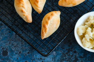 Small mashed potato pasties (hand pies) in a wire rack. Blue stone background.