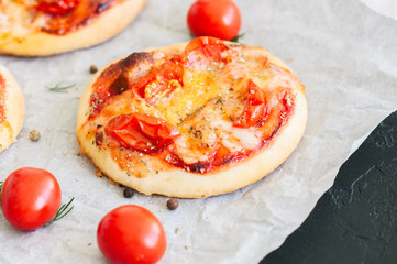 Mini pizzas margheritas served on a baking paper. Black stone background.