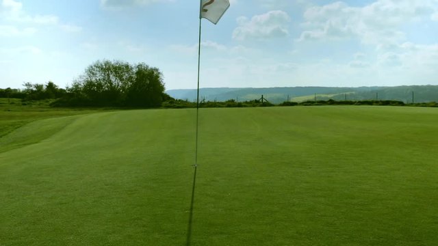 Pan shot of a green golf course, hole and flag on a bright sunny day. Sport, relax, recreation and leisure concept. Summer landscape with sunbeams
