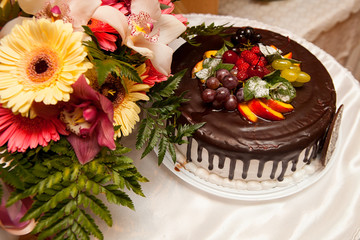A festive cake beautifully decorated with fruits against a bouquet of flowers