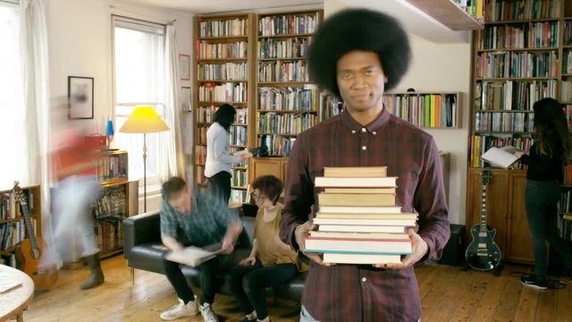 Time lapse students in shared home, man stands still while his friends pile him with books
