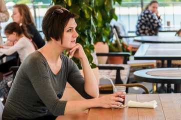 Beautiful woman with short hairdo sits on a summer terrace at a cafe and drinks a cocktail