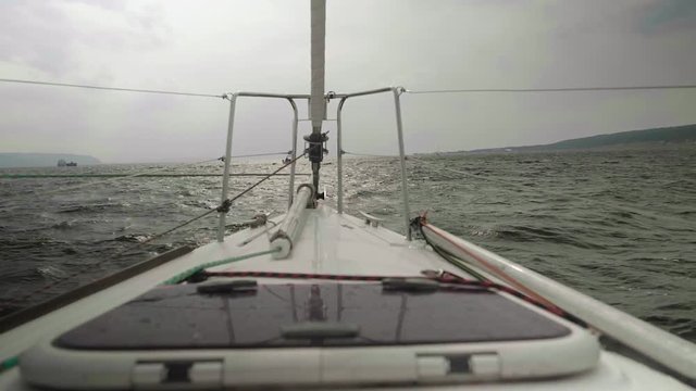 Slow motion view of coastline, stormy water of river and boats on it. View from sailing yacht board
