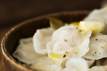 Close up fresh cooked russian dumplings with melting butter and ground pepper in wooden palte on table. Text space