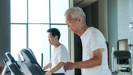 Fototapeta na wymiar Healthy Asian senior couple exercise together in gym running treadmill