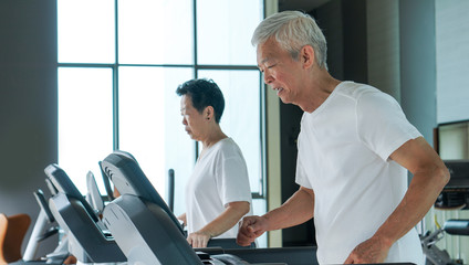 Healthy Asian senior couple exercise together in gym running treadmill