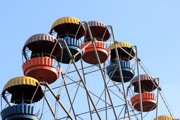 Colorful ferris wheel slowly moving against blue sky in the summer amusement park