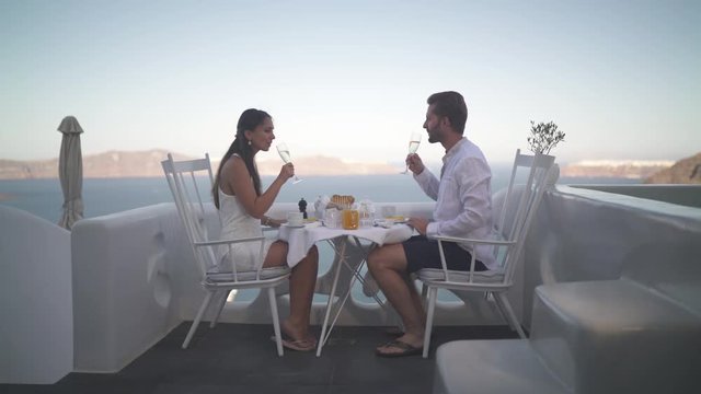 4k travel video honeymoon couple having breakfast with champagne on private terrace outside their hotel room overlooking the caldera on santorini island greece
