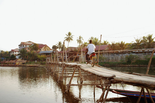 A man riding a motorbike over a wooden bridge in local village asian style. vintage image.