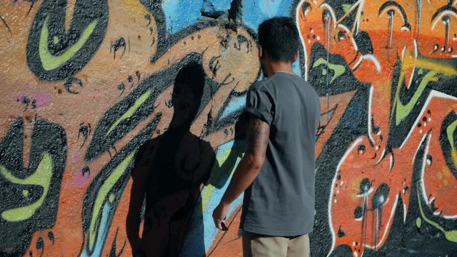 Handsome Talented Young Boy making a colorful graffiti with aerosol spray on urban street wall. Cinematic toned slow motion footage. Creative art.