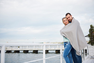 Beautiful young couple embracing, standing on a pier near water