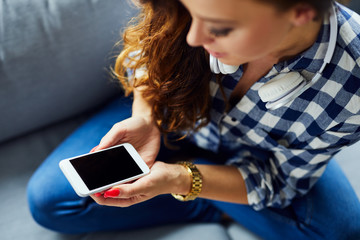 HIgh angle shot of a young woman sitting on sofa and using phone, showing screen