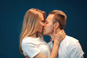 A loving couple is kissing and posing in the studio. Love between a young man and a beautiful woman.