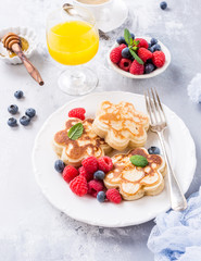Scotch pancakes in flower form with berries and honey on white wooden background. Healthy breakfast concept.