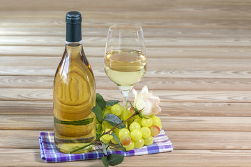 Bottle and glass of white wine are stand on table together with rose