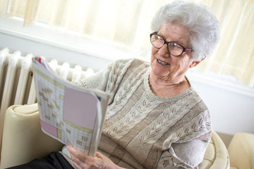 Happy senior woman solving crossword puzzle at home.