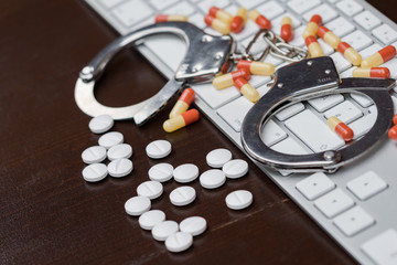 Handcuffs and pills over computer keyboard