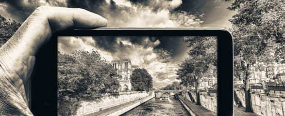 Male hand with smartphone taking a picture of Paris and Notre Dame. Tourism concept