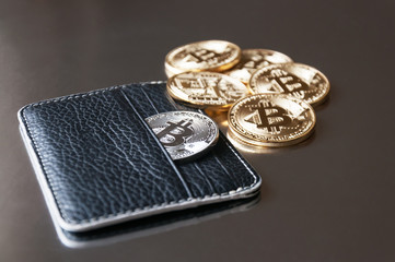 The black leather wallet on a dark background with several gold and silver coins of bitcoins falling out of their pockets. The concept of crypto currencies.