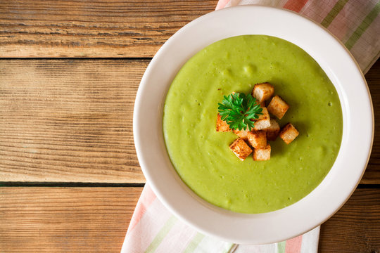 Broccoli cream soup with croutons in plate on rustic wooden table