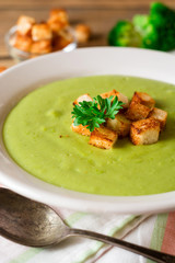 Broccoli cream soup with croutons in plate on rustic wooden table